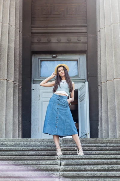 Young beautiful woman in straw hat standing on steps on street — Stock Photo