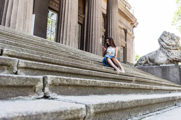 Mujer joven usando el teléfono inteligente mientras descansa en los escalones de la calle - foto de stock