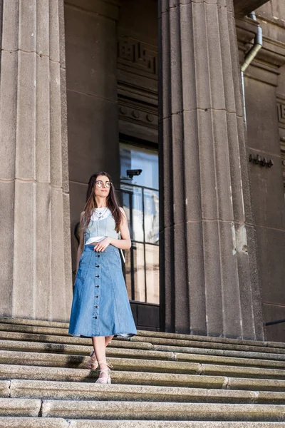 Молода стильна жінка в окулярах і джинсова спідниця стоїть на сходах — стокове фото