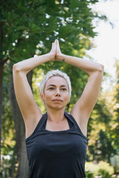 Mujer practicando yoga con las manos en gesto namaste en parque - foto de stock