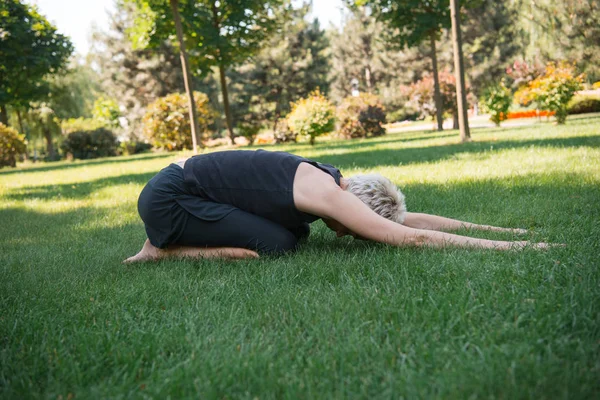 Vista lateral de la mujer practicando yoga en pose de niño extendido (Utthita Balasana) sobre hierba en parque - foto de stock