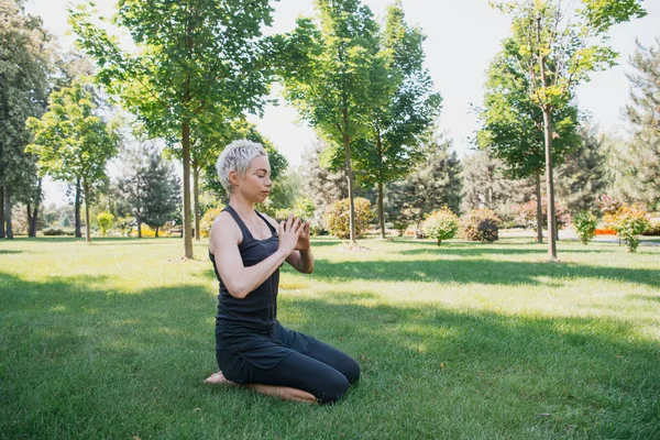 Frau praktiziert Yoga und macht Geste mit den Händen auf Gras im Park — Stockfoto
