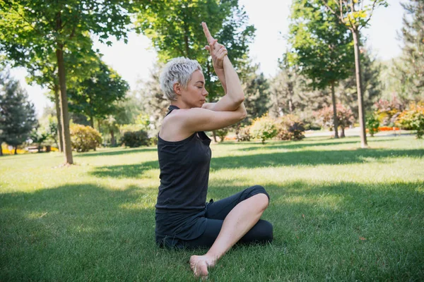 Vista lateral de la mujer practicando yoga y sentada sobre hierba en el parque - foto de stock