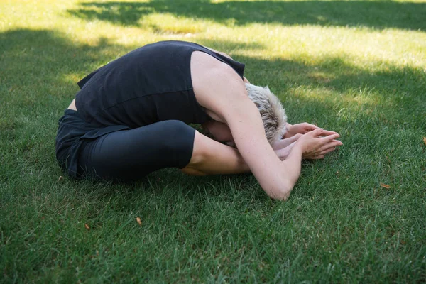 Side view of woman practicing yoga on grass in park — Stock Photo