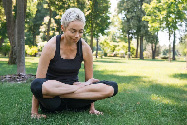 Mujer deportiva practicando yoga en pose de loto y sosteniendo el cuerpo en las manos en el parque - foto de stock