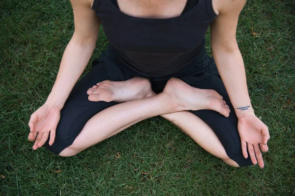 Imagen recortada de la mujer practicando yoga en pose de loto y meditando sobre hierba en parque - foto de stock
