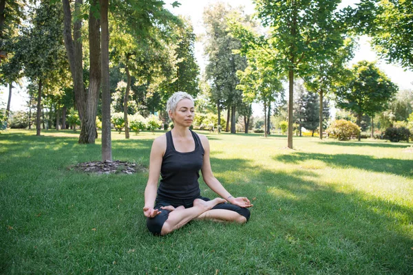 Mulher praticando ioga em pose de lótus e meditando na grama no parque — Fotografia de Stock