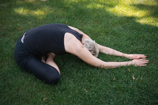 Seitenansicht einer Frau, die Yoga in breiter Kinderpose (Balasana) auf Gras im Park praktiziert — Stockfoto