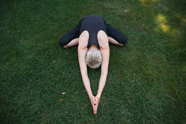 Vista de ángulo alto de la mujer practicando yoga en pose de niño ancho (Balasana) sobre hierba en parque - foto de stock