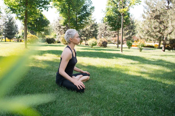 Vista lateral de la mujer practicando yoga en pose de loto sobre hierba en parque - foto de stock