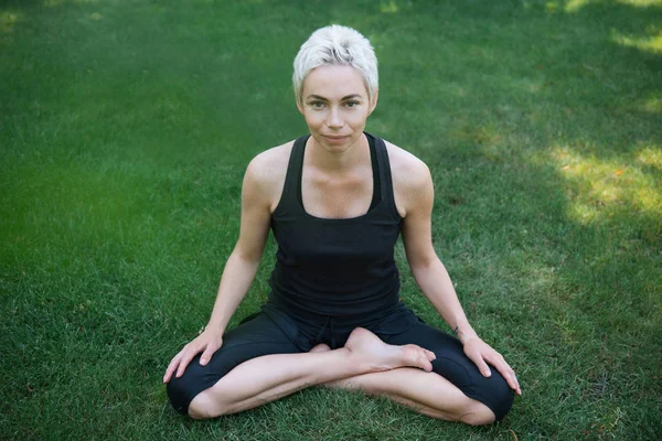 Woman practicing yoga in lotus pose on green grass in park — Stock Photo