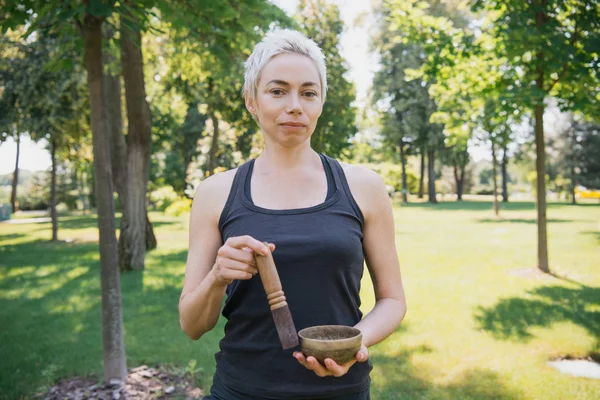 Frau macht Geräusche mit tibetischer Klangschale im Park und blickt in Kamera — Stockfoto