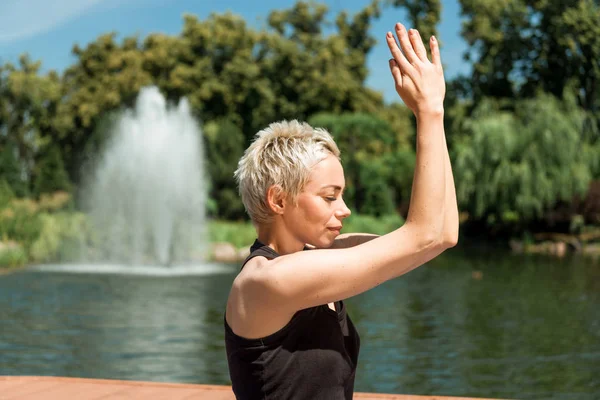 Vista lateral de la mujer practicando yoga con las manos en gesto namaste cerca del río en parque - foto de stock