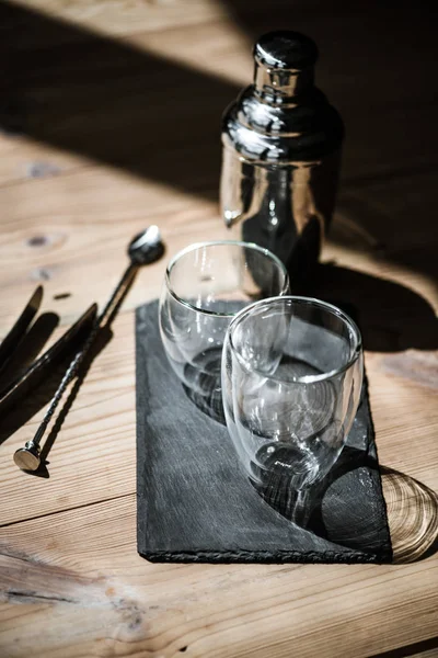 Vista de cerca de vasos vacíos en pizarra, agitador y pinzas en mesa de madera - foto de stock