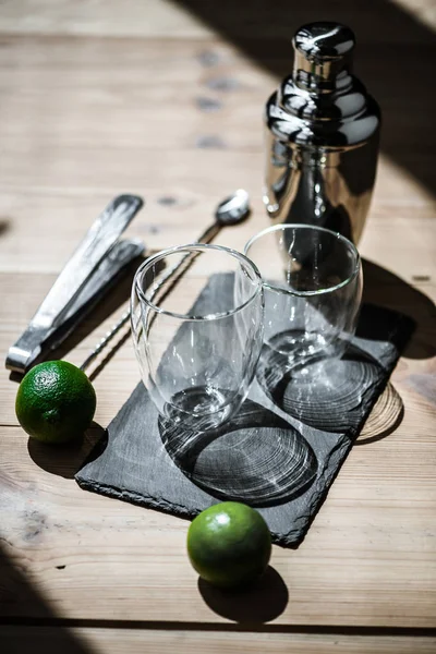 Vista close-up de limas frescas, copos vazios, pinças e coqueteleira na mesa de madeira — Fotografia de Stock