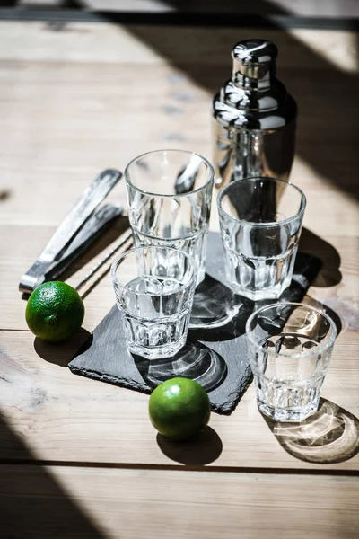 Vue grand angle des chaux fraîches, verres vides, pinces et shaker sur table en bois — Photo de stock