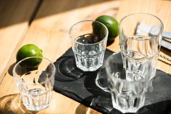 Vue rapprochée de verres vides, pinces et citrons verts frais sur table en bois — Photo de stock