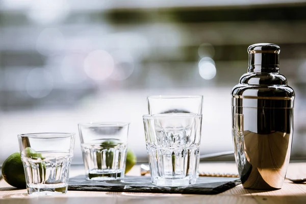Vista close-up de shaker brilhante, vidros vazios e limas frescas na mesa de madeira — Fotografia de Stock