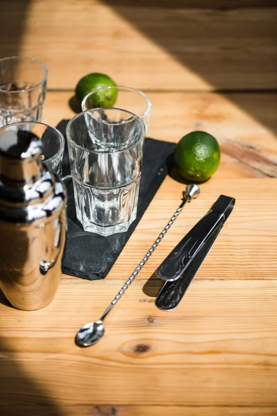 Vue grand angle des verres vides, shaker, pinces et chaux fraîches sur table en bois — Photo de stock