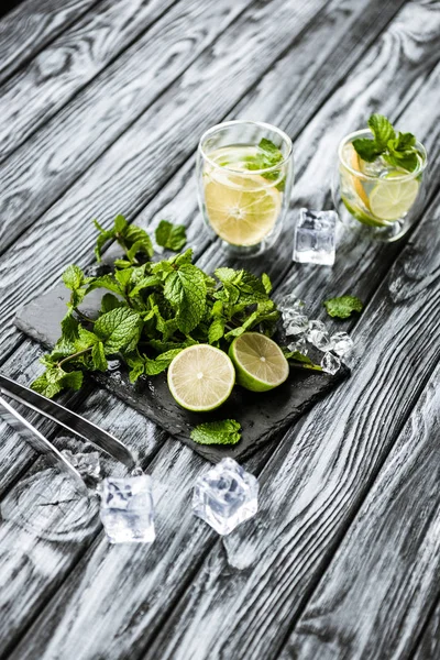 Высокий угол обзора летнего коктейля в стаканах и ингредиентах для приготовления мохито на деревянном столе — стоковое фото