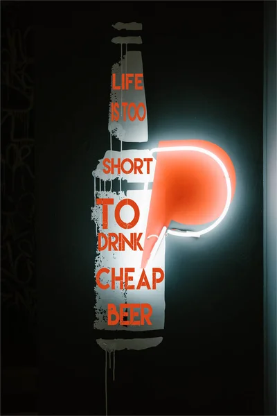 Illuminated beer bottle symbol on dark wall in pub with 