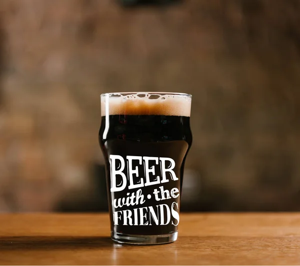 Glass of fresh cold dark beer on wooden table in pub with 