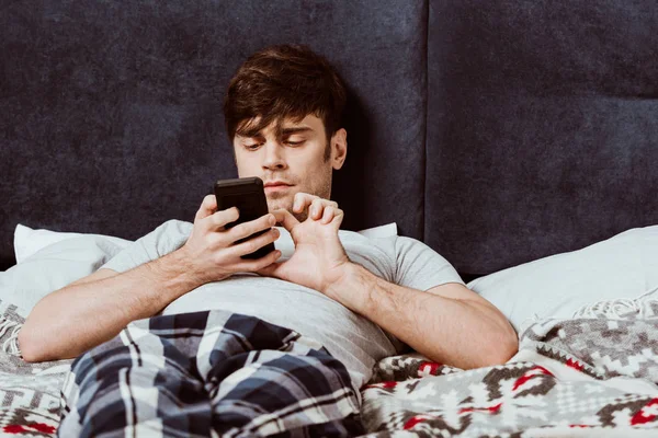 Enfoque selectivo del hombre usando el teléfono inteligente mientras está acostado en la cama en casa - foto de stock