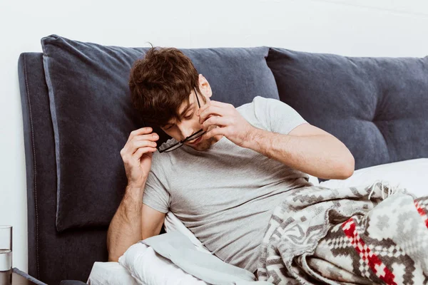 Man waking up and putting on eyeglasses during morning time in bed at home — Stock Photo