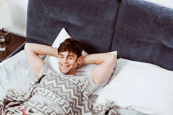 Высокий угол зрения улыбающегося человека, лежащего в постели в утреннее время дома — стоковое фото