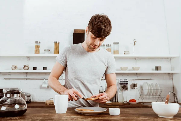 Schöner Mann verteilt Toast von Marmelade in Küche zu Hause — Stockfoto