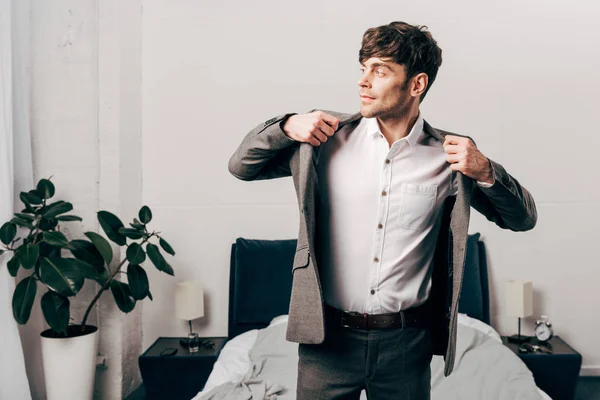 Vista lateral del hombre de negocios guapo que se pone la chaqueta en el dormitorio en casa - foto de stock