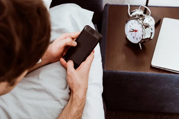 Visão parcial do homem usando smartphone com tela em branco enquanto deitado na cama em casa — Fotografia de Stock