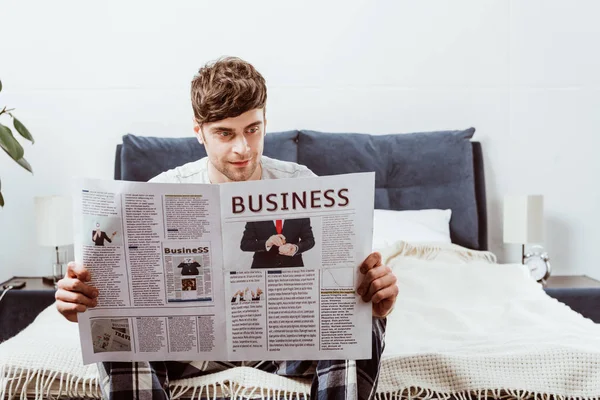 Lächelnder Mann, der zu Hause im Bett die Wirtschaftszeitung liest — Stockfoto