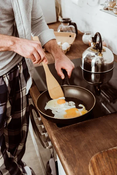 Imagen recortada del hombre cocinando huevos revueltos en la sartén en la cocina - foto de stock