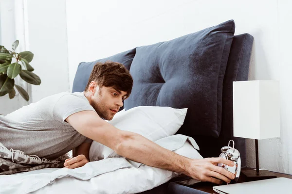 Selective focus of young man turning off alarm clock in bed at home — Stock Photo