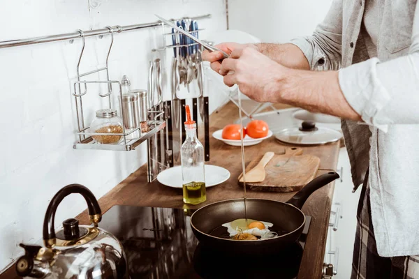 Partial view of young man cooking scrambled eggs on breakfast in kitchen — Stock Photo