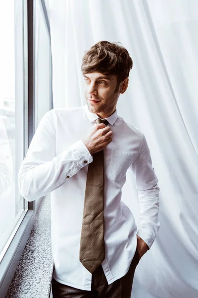 Smiling businessman in white shirt tying neck tie in office — Stock Photo