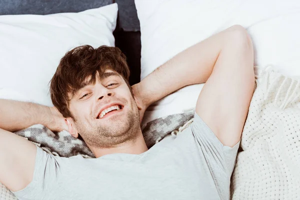 Porträt eines jungen Mannes, der morgens zu Hause in die Kamera schaut und im Bett liegt — Stockfoto