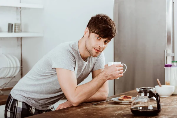 Man drinking coffee at table with toasts and coffee pot in kitchen at home — Stock Photo