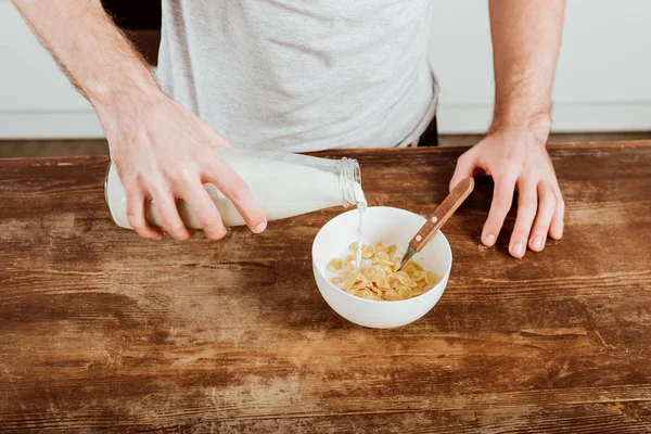 Immagine ritagliata di uomo versare il latte in ciotola con fiocchi di mais a tavola con computer portatile in cucina a casa — Foto stock