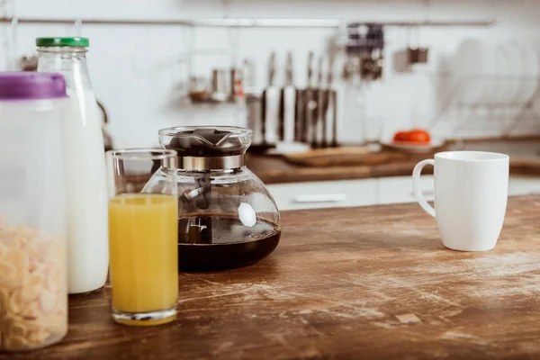 Enfoque selectivo de copos de maíz, taza de café y jugo de naranja en la mesa de madera en la cocina - foto de stock