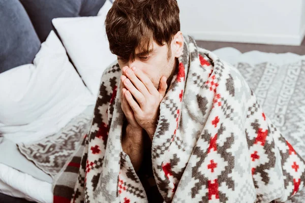 Селективное внимание больного молодого человека, завернутого в одеяло, сидящего дома на кровати — стоковое фото