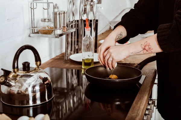 Imagen recortada de la mujer con la mano tatuada haciendo huevos en el desayuno en casa - foto de stock