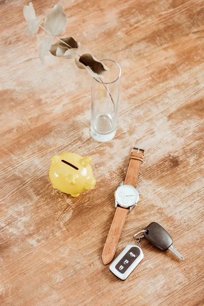Vue grand angle de la clé de voiture à distance, montre, tirelire et branche à la table en bois — Photo de stock