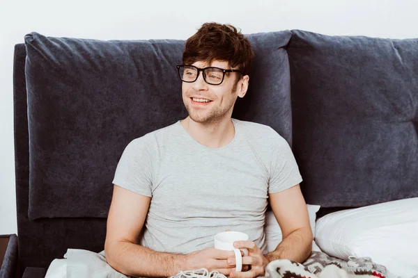 Sorrindo jovem deitado na cama com xícara de café em casa — Fotografia de Stock