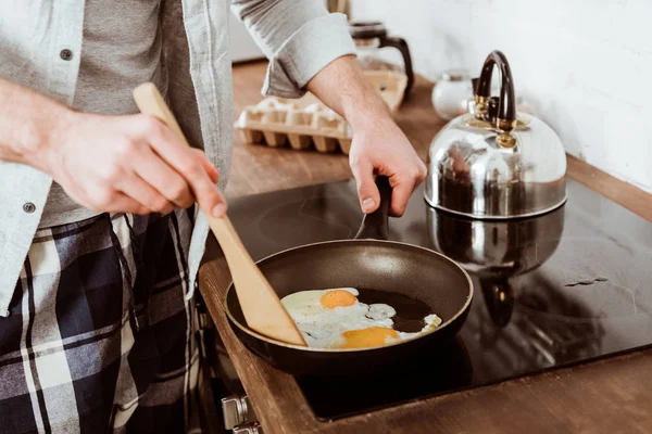 Partial view of man cooking scrambled eggs on frying pan in kitchen — Stock Photo