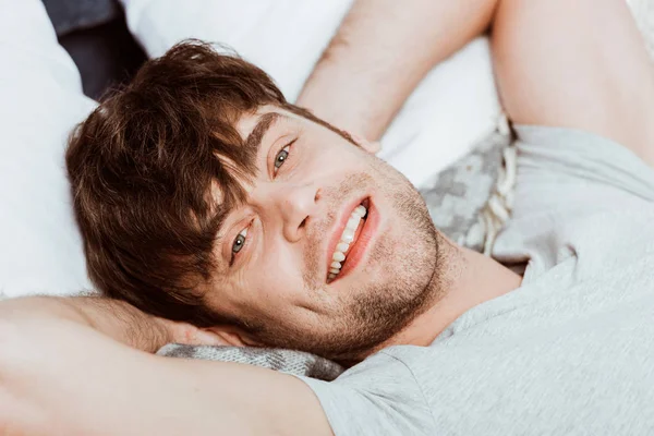 Close up portrait of young man looking at camera and laying in bed during morning time at home — Stock Photo