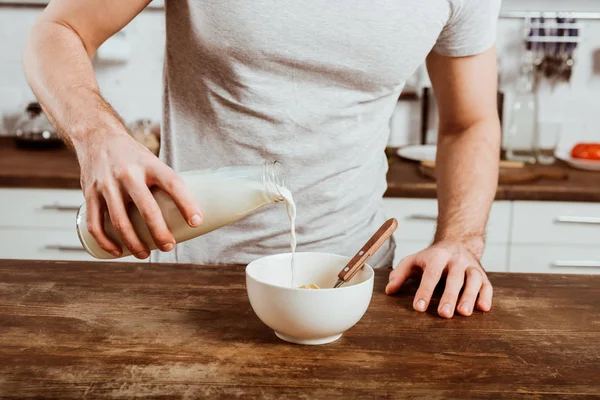 Обрезанный образ человека, наливающего молоко в миску с кукурузными хлопьями на кухне дома — стоковое фото