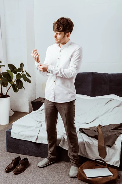 Junger hübscher Geschäftsmann knöpft sich weißes Hemd im Schlafzimmer zu Hause zu — Stockfoto