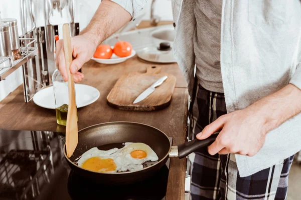 Imagen recortada de un joven cocinando huevos en la sartén en la cocina - foto de stock